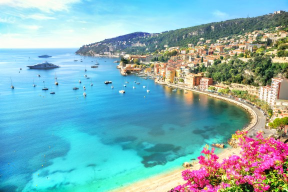 View of Nice coastline in France, with blue water and lots of boats and a huge superyacht. Pink flowers in the foreground gives the picture a warm and summerly feel.